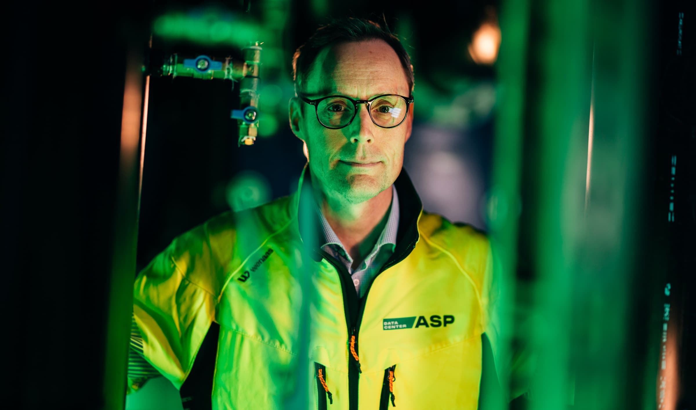 Engineer inspecting equipment in a green-lit data hall
